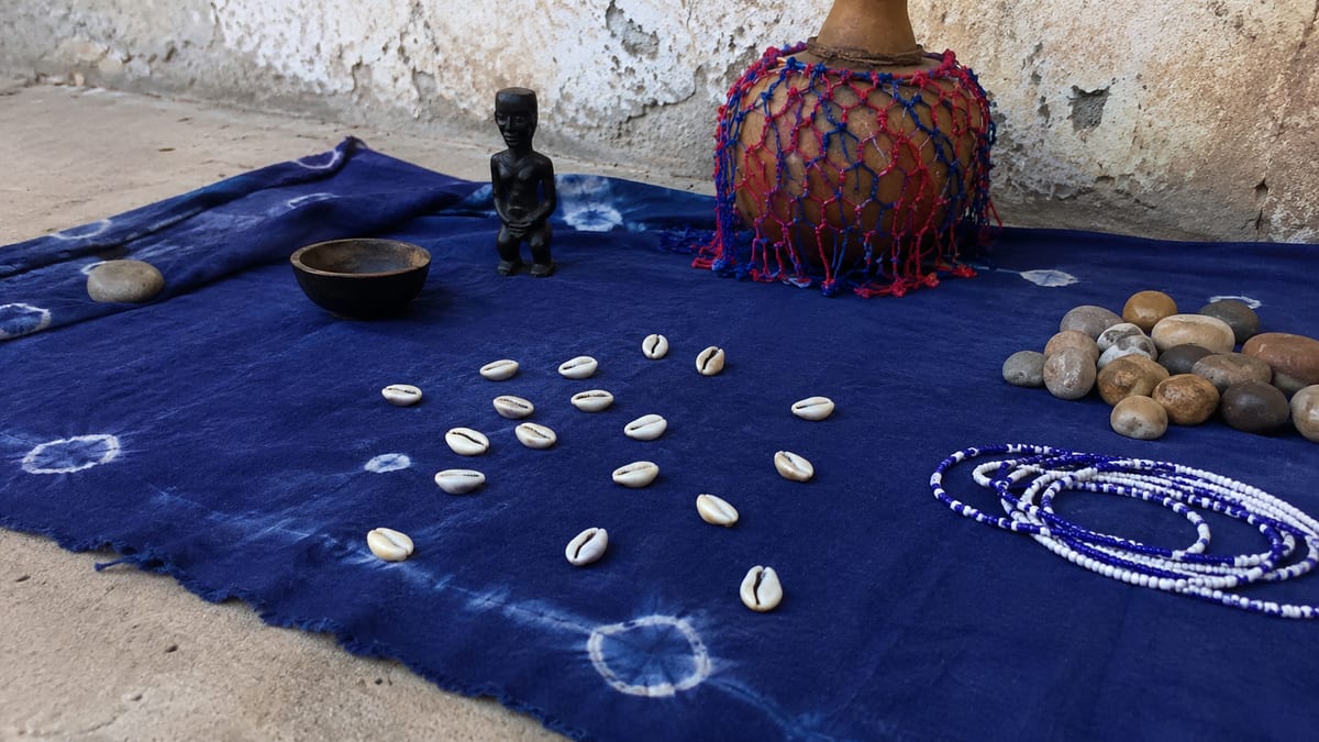 Étoffe indigo posée au sol, cauris disposés en figure de divination et statuette de bois